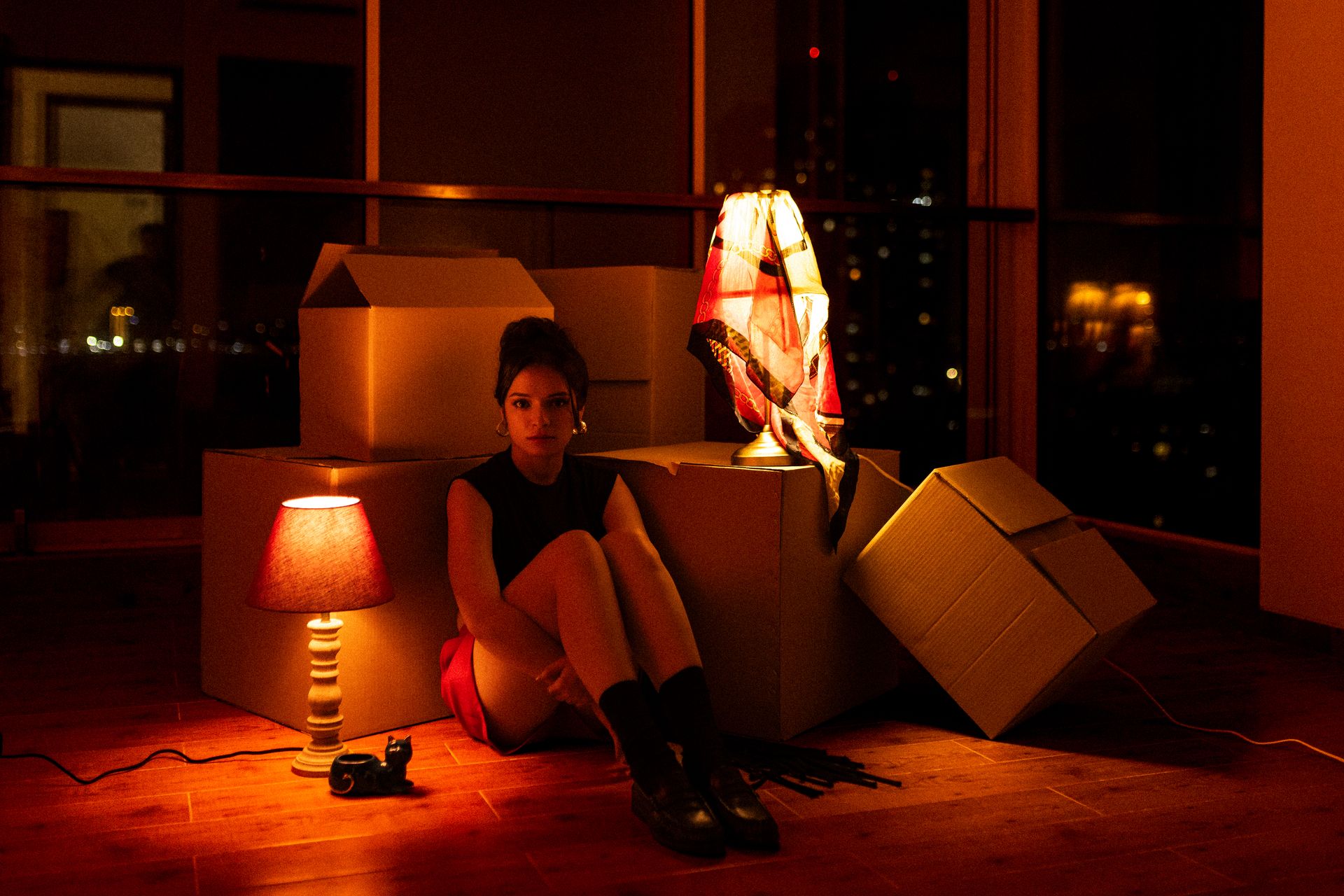 Mali sitting among packing boxes by a window at night